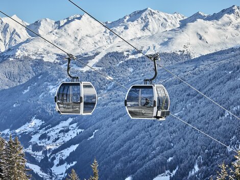 Ein Skifahrer fährt über eine schneebedeckte Piste in den Bergen. Im Hintergrund sind majestätische Berge und ein klarer Himmel zu sehen.