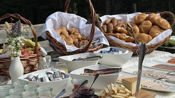 A rich breakfast buffet with baskets full of rolls and pastries.  
There are various jams and many little treats on a beautifully set table.
