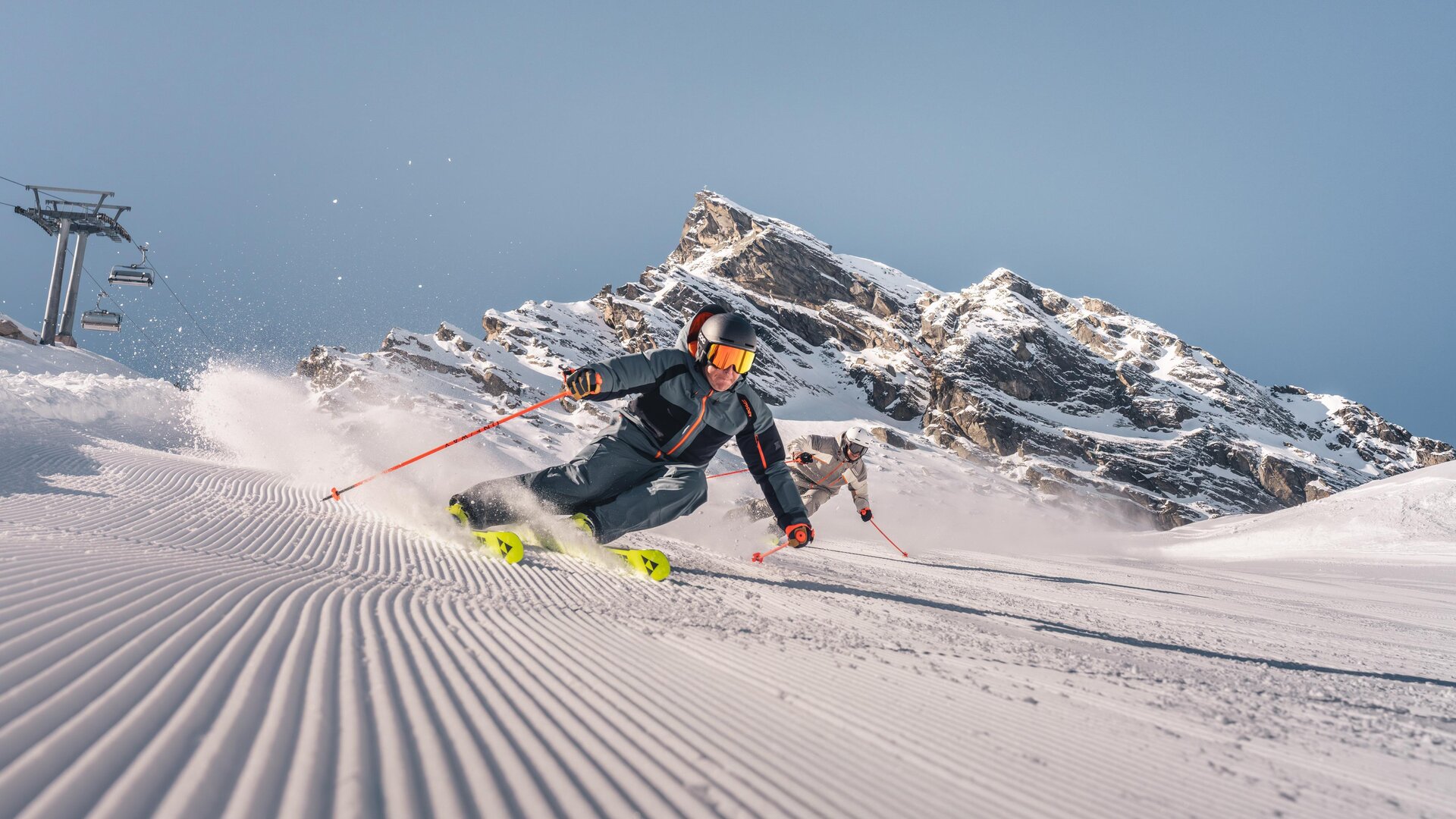 A skier glides through fresh snow in the mountains. In the background, impressive rocks and a blue sky can be seen.