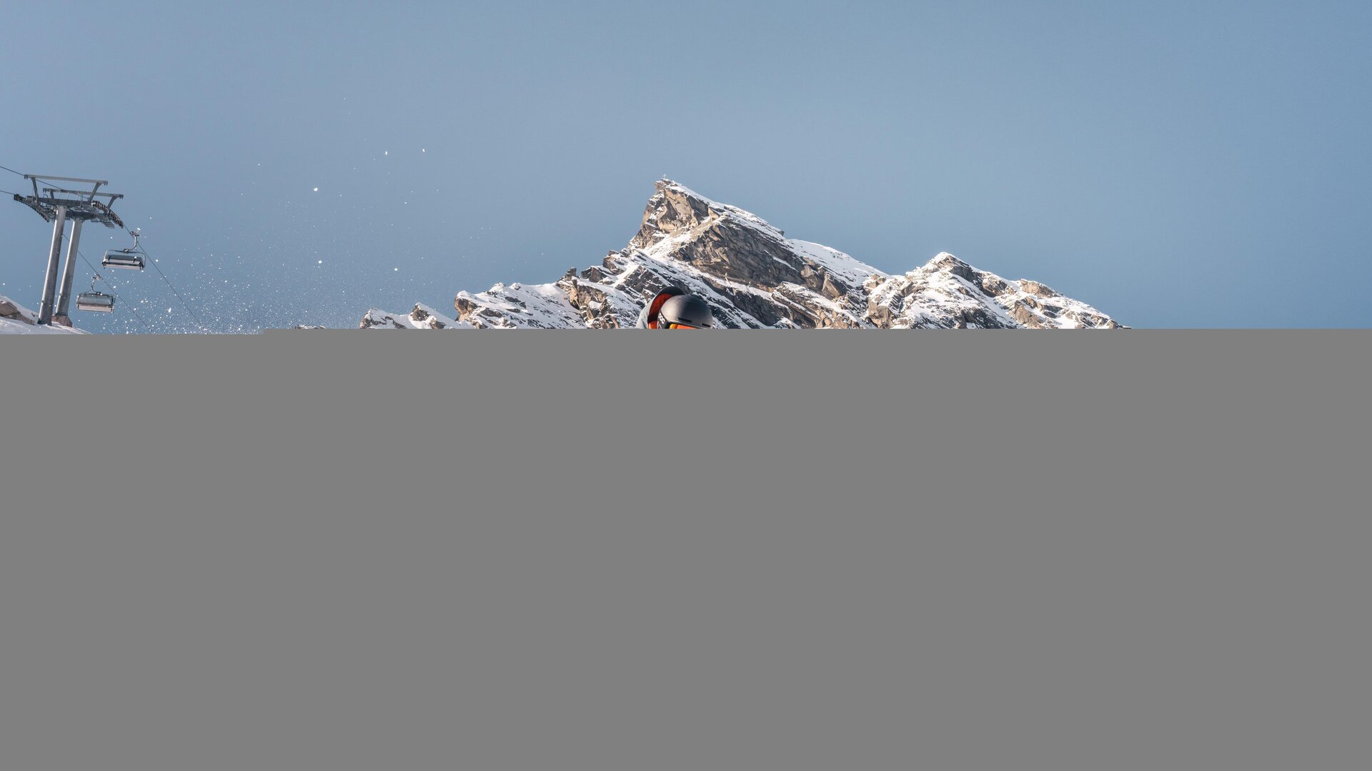 A skier glides through fresh snow in the mountains. In the background, impressive rocks and a blue sky can be seen.