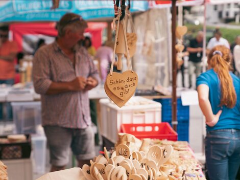 A market stand with handcrafted wooden items. In the background, people can be seen examining the offerings.