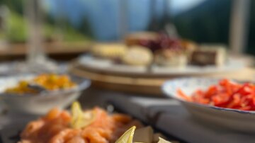 A deliciously arranged fish dish with lemon and various side dishes. In the background, mountains and a clear sky are visible.