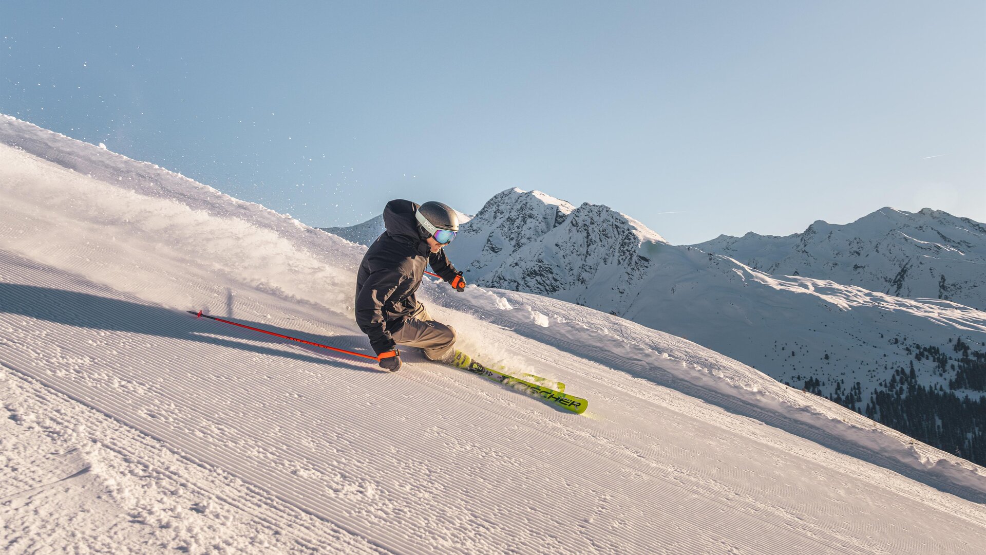 A skier is going down a snowy slope. In the background, snow-covered mountains can be seen.