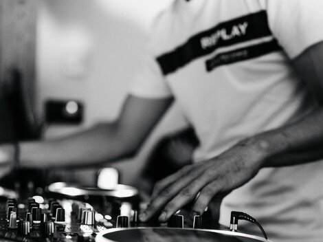 Ein DJ, der an einem Mischpult arbeitet. Die Atmosphäre ist dynamisch und energiegeladen.
