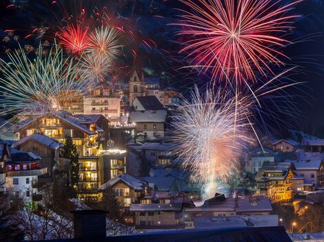 A festive scene with colorful fireworks over a snow-covered village. The houses shine in the light of the fireworks, creating a festive atmosphere.