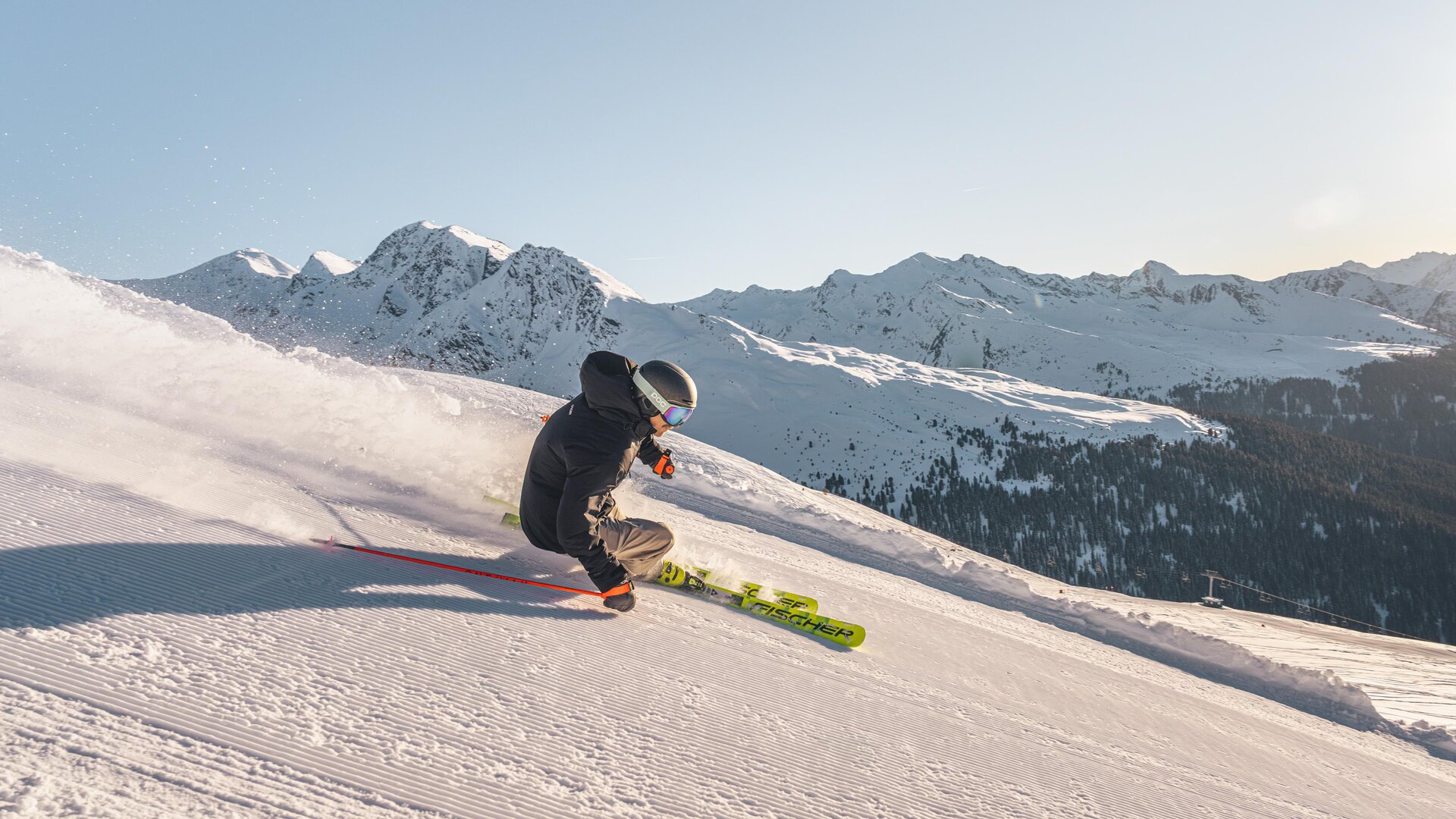 A skier glides over a snow-covered slope in the mountains. In the background, majestic mountains and a clear sky can be seen.