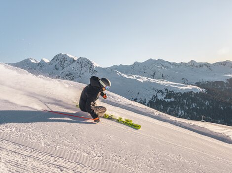 A skier is going down the snow-covered slope. In the background, majestic mountains are visible.