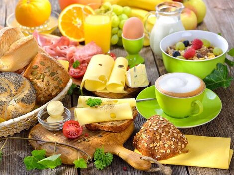 Ein reichhaltiges Frühstück mit verschiedenen Brotsorten, buntem Obst und Getränken. Dazu gibt es Käse und Joghurt in appetitlichen Schalen.