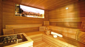 Eine moderne Sauna mit Holzverkleidung und Bänken. Ein großes Fenster zeigt eine malerische Landschaft mit Bergen.
