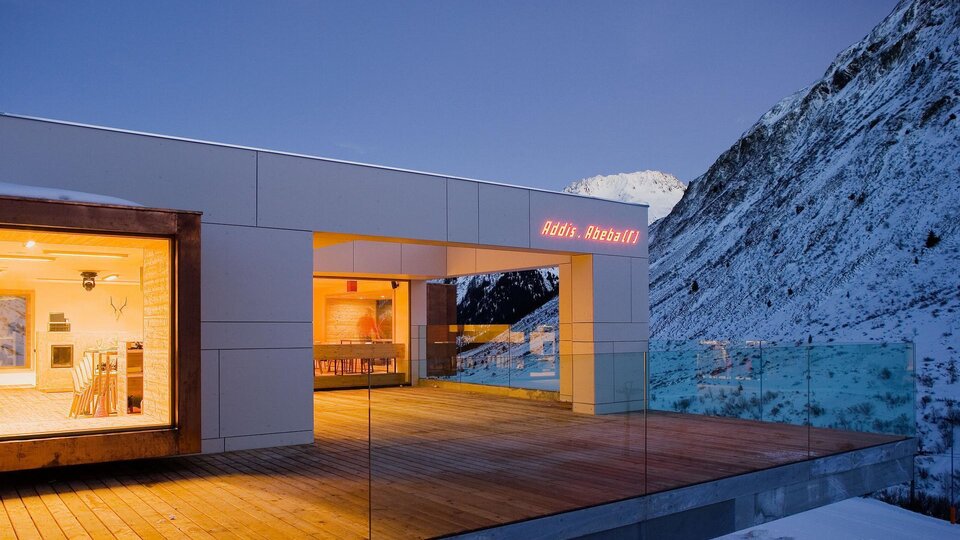 Ein modernes Haus in den Bergen, umgeben von Schnee. Der Balkon bietet einen herrlichen Blick auf die umliegenden Berge.