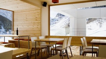 Ein modernes Restaurant mit holzverkleideten Wänden und großen Fenstern. Der Blick auf die verschneiten Berge schafft eine gemütliche Atmosphäre.