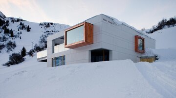 Ein modernes Gebäude in einer schneebedeckten Landschaft. Die Umgebung zeigt Berge und klare Himmel.