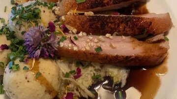 Ein köstliches Gericht mit gebratenem Fleisch, garniert mit Kräutern und essbaren Blumen. Dazu gibt es eine Beilage aus Kartoffel und Sauce.
