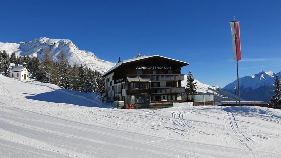 A beautiful chalet in a snowy mountain landscape. Clear blue skies and surrounding coniferous trees.