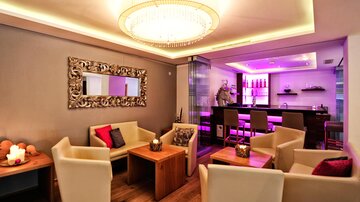 A modern lounge room with comfortable armchairs and an elegant table. The soft lighting and the colorful accents create an inviting atmosphere.