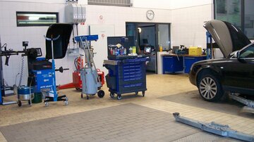 A workshop with various tools and machines. A car is in the corner, while the floor is tiled.
