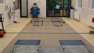 Eine moderne Autowaschanlage mit einem offenen Bereich und mehreren Waschstationen. Der Boden ist gepflastert und es gibt verschiedene Geräte zur Fahrzeugreinigung.