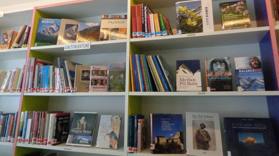 Ein Bücherregal mit vielen verschiedenen Titeln, das das Wort „TIROL“ oberhalb zeigt. Die Bücher umfassen verschiedene Themen und Genres.