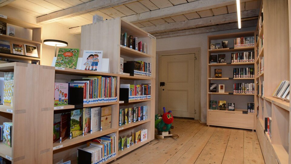 A bright room with wooden shelves containing many books. In one corner, there is a toy, and the light is pleasant.