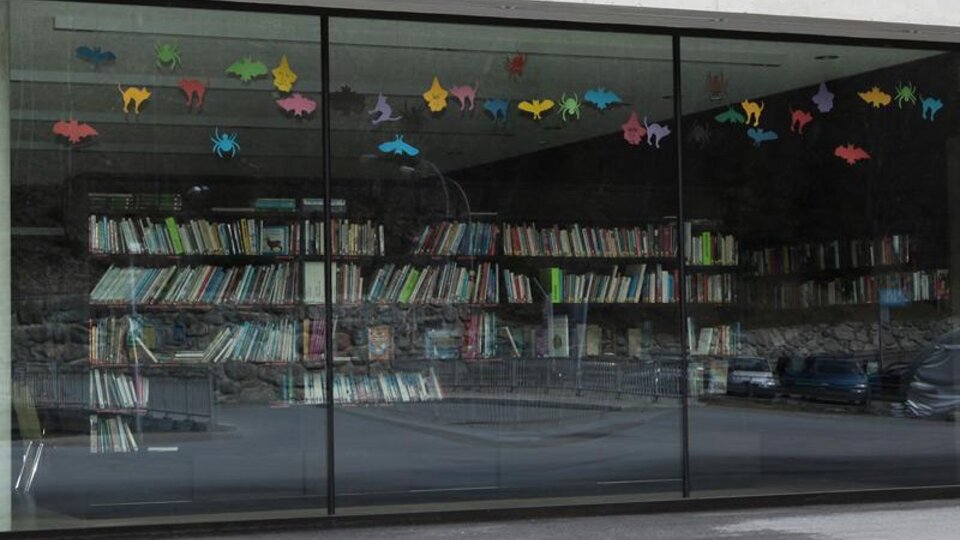 A modern window with colorful animal motifs that looks out onto a wall of books. The books are neatly arranged on shelves.