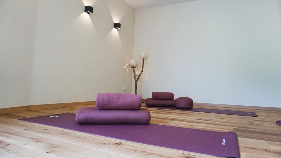 A tranquil yoga room with purple mats sits on a wooden floor. Soft light creates a relaxing atmosphere.