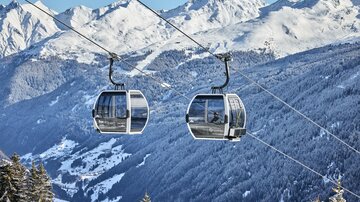 Zwei Gondeln auf einer Seilbahn über schneebedeckte Berge. Die Landschaft ist winterlich und majestätisch.