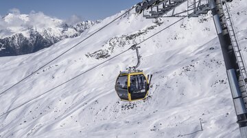 Eine Seilbahn schwebt über eine schneebedeckte Landschaft. Im Hintergrund sind majestätische Berge sichtbar.