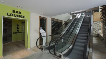 Ein moderner Eingangsbereich mit einer Rolltreppe und einem Bereich für die Bar-Lounge. Die Wände sind in hellen Farben gehalten und sorgen für eine einladende Atmosphäre.