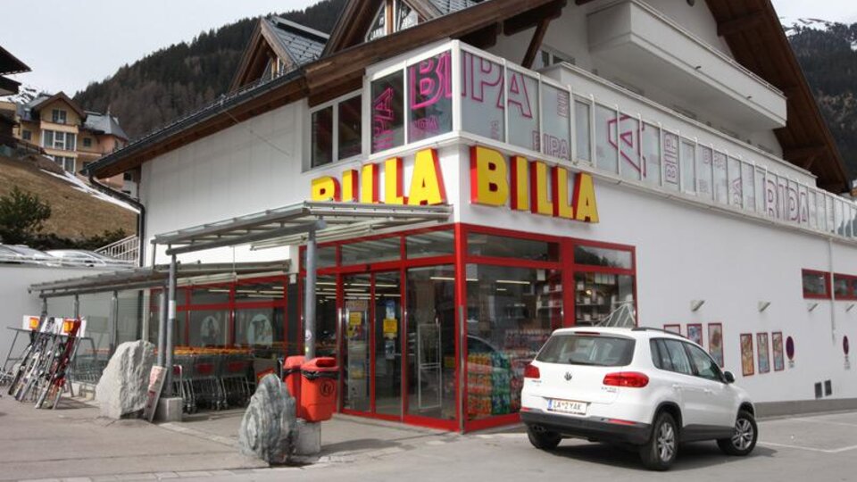 Ein Billa-Supermarkt mit einer modernen Fassade und großen Fenstern. Vor dem Geschäft steht ein weißes Auto auf einem Parkplatz.