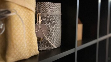 Zwei dekorative Taschen in Gelb und Grau stehen auf einem Regal. Im Hintergrund sind weitere Regalfächer sichtbar.