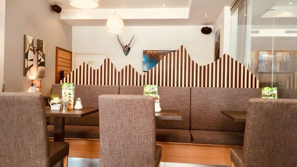 Ein modernes Restaurant mit gemütlichen Sitzecken und einer dekorativen Wand im Bergdesign. Das Licht ist hell und freundlich, was eine einladende Atmosphäre schafft.