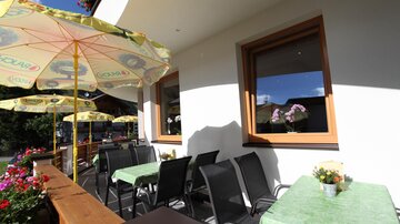 An inviting terrace with tables and chairs. Umbrellas provide shade and flowers adorn the space.