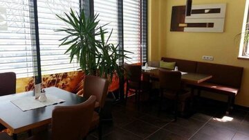 A cozy restaurant with modern furniture and large windows. The bright colors and plants create an inviting atmosphere.