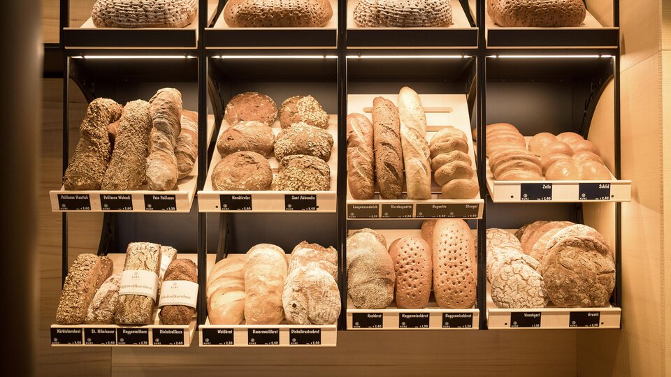 Eine Auswahl an frischem Brot in verschiedenen Formen und Farben. Die Brote sind ordentlich in Regalen angeordnet.