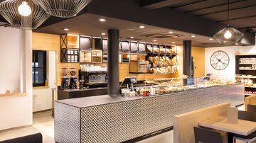Ein modernes Café mit einer eleganten Theke und einer Auswahl an frischen Backwaren. Die Atmosphäre ist hell und einladend.