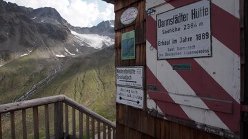 A mountain cabin with a view of the surrounding mountains and glaciers. The cabin features a wooden design and several informative signs.