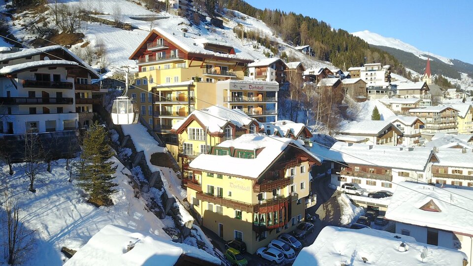 Eine malerische Winterlandschaft mit schneebedeckten Dächern und traditionellen Holzgebäuden. Die Berge im Hintergrund vervollständigen das idyllische Bild.