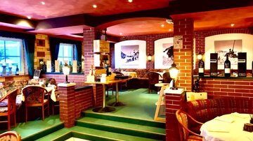 Ein gemütliches Restaurant mit einer warmen Atmosphäre. Der Raum ist mit rot-steinernen Wänden und komfortablen Tischen ausgestattet.