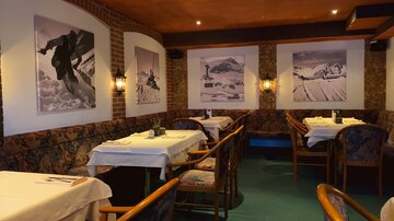 Ein gemütliches Restaurant mit Holzmöbeln und Tischen, die mit weißen Tischdecken bedeckt sind. An den Wänden hängen beeindruckende Schwarz-Weiß-Fotos von Berglandschaften.