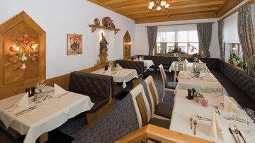 Ein gemütliches Restaurant mit Holzmöbeln und elegant gedeckten Tischen. Große Fenster lassen viel Licht herein und schaffen eine einladende Atmosphäre.