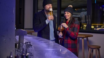 A couple is standing at a bar enjoying drinks. Both are wearing warm hats and the atmosphere is cozy.