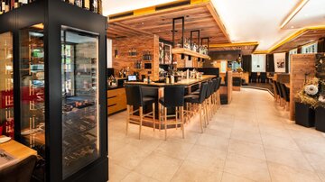 A modern bar with wooden details and a long counter. Behind the counter are wine bottles and there are cozy seating areas.