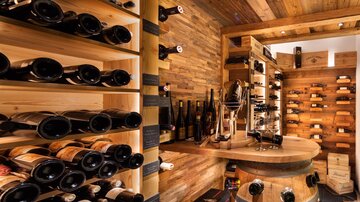 A stylishly furnished wine cellar with a wooden shelf full of wine bottles. In the middle stands a round table made from a wine barrel.
