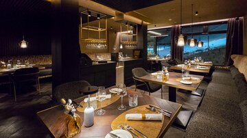 Ein elegantes Restaurant mit modernen Tischen und Stühlen. Die Atmosphäre ist gemütlich und stilvoll, mit Blick auf eine panoramische Aussicht.