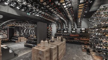 Ein stilvoll eingerichteter Weinkeller mit Regalen voller Weinflaschen. In der Mitte stehen Holzkisten und Kerzen schaffen eine gemütliche Atmosphäre.