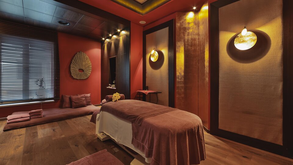 Ein stilvolles Spa-Zimmer mit einer Massageliege und sanfter Beleuchtung. Die Wände sind in warmen Farbtönen gehalten und schaffen eine entspannende Atmosphäre.