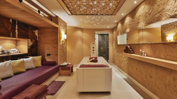 Ein eleganter Spa-Raum mit beruhigenden Farben und einem entspannenden Ambiente. Es gibt eine Massageliege und gemütliche Sitzgelegenheiten.