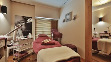 Ein stilvolles Wellnesszimmer mit bequemen Behandlungsliegen und kosmetischen Utensilien. Die Wände sind in sanften Farben gehalten und schaffen eine entspannende Atmosphäre.