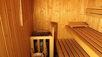 A cozy sauna with wooden-paneled walls and benches. A bucket and a ladle are ready for the infusion.