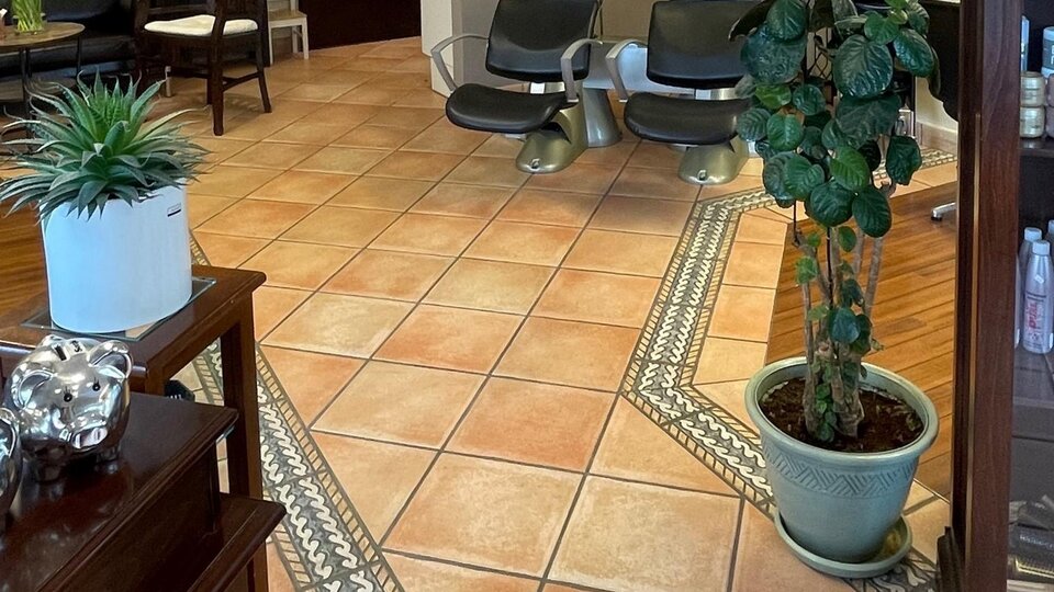 Ein Salon mit modernen Friseurstühlen und Waschbecken. Die Wände sind mit Bildern und einer Pflanze dekoriert.